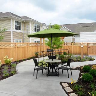 A cozy patio setup with an outdoor table, chairs, and a green umbrella in a landscaped garden area.
