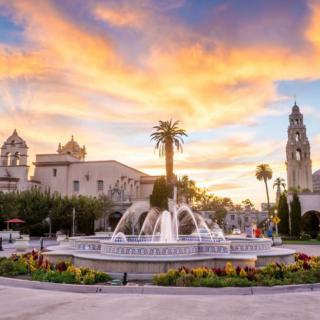 A beautiful sunset over a historic fountain surrounded by palm trees and architectural buildings.
