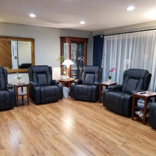 A cozy living room featuring a row of four black recliners, hardwood flooring, and soft lighting from a table lamp.