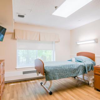 A well-lit hospital room featuring a bed, a television, and light wooden furniture.