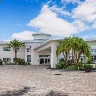 A modern building with palm trees and a spacious driveway under a blue sky with clouds.