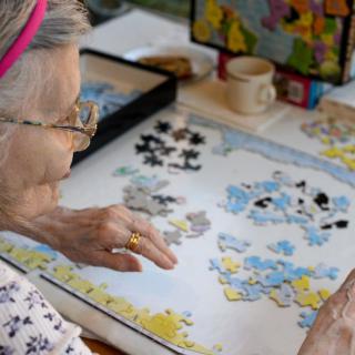 An elderly person working on a jigsaw puzzle at a table.