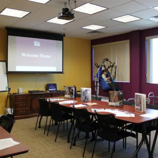 An empty conference room set up for a meeting or presentation, featuring a projector screen and neatly arranged tables and chairs.