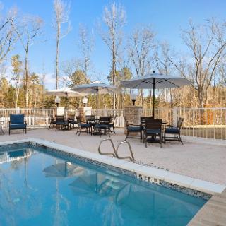 A serene outdoor swimming pool area featuring patio furniture and umbrellas under a clear blue sky.