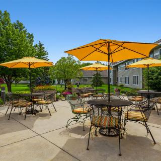 Outdoor patio area with tables and yellow umbrellas in a garden setting on a sunny day.