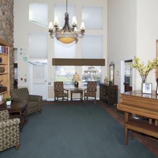 A spacious living room with a chandelier, piano, and comfortable seating arrangements.