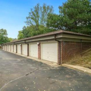 A row of brick garages along a paved driveway surrounded by trees.