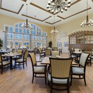A spacious and elegantly designed dining room with multiple tables and chairs, featuring large windows and stylish chandeliers.