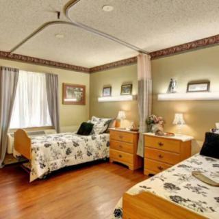 A cozy shared bedroom with two beds and warm lighting, likely in a nursing home or care facility.