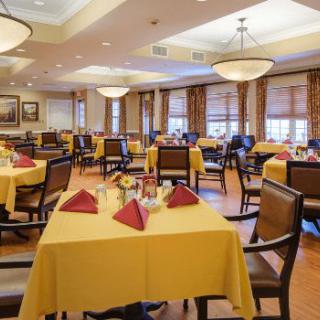 A spacious dining area with neatly arranged tables covered in yellow tablecloths and folded napkins.