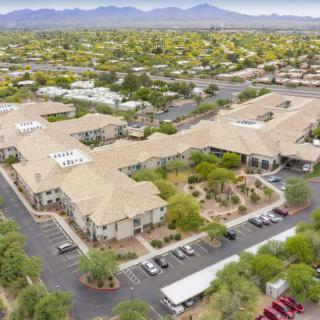 An aerial view of a residential complex with parking areas, surrounded by trees and set against a mountainous desert backdrop.