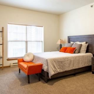 A modern bedroom with orange accents featuring a comfortable bed, a window with natural light, and stylish decor.