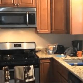 A kitchen with wooden cabinets, a stainless steel microwave and oven, and a cluttered countertop.