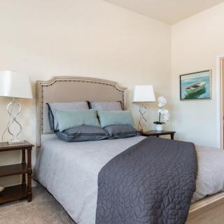 A cozy bedroom with a neatly made bed, nightstands, and lamps, accented by artwork on the wall.