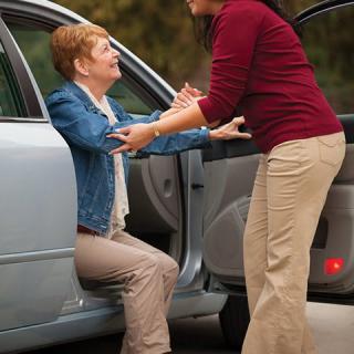 A woman helps an elderly person out of a car.
