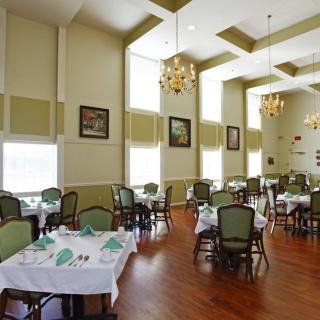 An elegant dining room with neatly set tables and chairs, complete with chandeliers and a warm wooden floor.