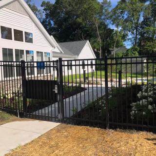 A residential house with a black metal fence and gate, featuring a concrete pathway leading to the entrance.
