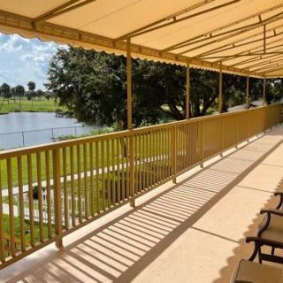 A sunny balcony with seating overlooking a lake and trees, sheltered by an awning.