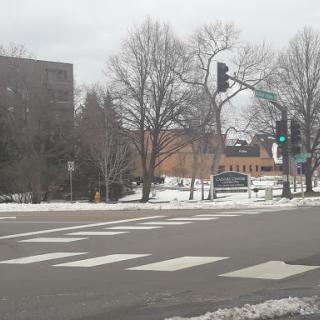 A snowy urban intersection with traffic lights and nearby buildings.