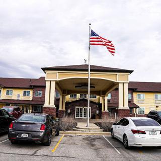 The entrance of a hotel with cars parked in front and an American flag flying above.