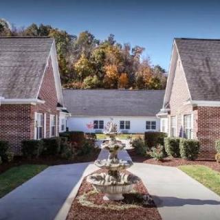 A quaint courtyard flanked by brick residential buildings, featuring a central fountain and surrounded by lush autumn foliage.