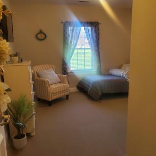 A cozy bedroom with a single bed, an armchair, and a window letting in natural light.
