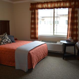 A cozy bedroom with an orange-themed decor, featuring a bed, bedside table, and a window with plaid curtains.