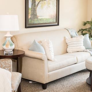 A cozy living room with a beige sofa, decorative pillows, a side lamp, and wall art.