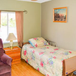 A cozy bedroom with a single bed featuring floral bedding, a bedside lamp, and curtains by the window.