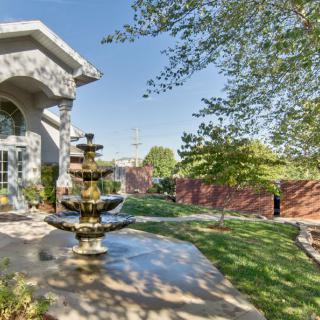 A tranquil patio area with a decorative fountain surrounded by trees and grass.