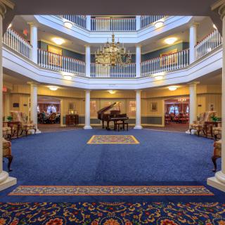A spacious hotel lobby with a central grand piano, surrounded by elegant columns and topped with a large chandelier.