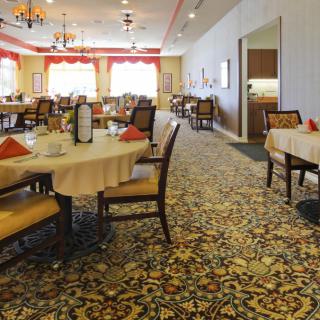 A spacious and elegantly decorated dining room with multiple tables and chairs arranged on a patterned carpet.