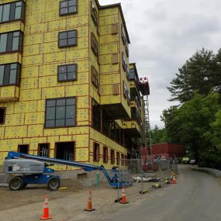 A construction site featuring a partially built multi-story building with yellow insulation and surrounding safety measures.