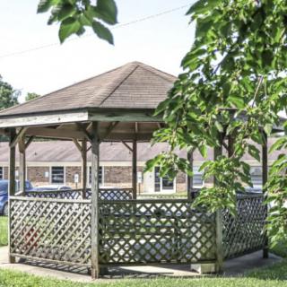 A wooden gazebo with lattice sides surrounded by trees and grass.