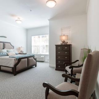A cozy bedroom with a bed, dresser, and chairs by the window.