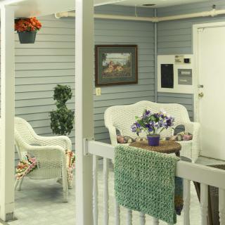 A cozy porch with white wicker furniture, colorful flowers, and a touch of greenery.