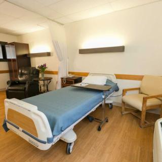 A clean and organized hospital room with a bed and chairs.