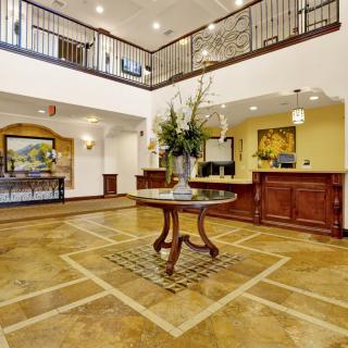 A spacious and elegant hotel lobby with a central table adorned with flowers, featuring warm lighting and classic interior decor.