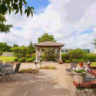 A serene garden setting featuring a central gazebo surrounded by patio chairs and lush greenery.