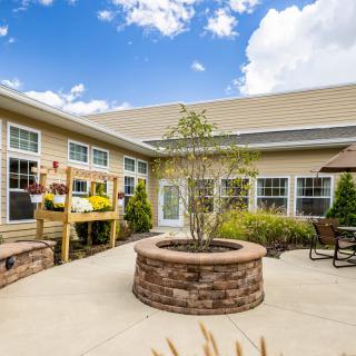 A sunny courtyard featuring a brick planter, patio furniture, and vibrant landscaping.