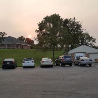 A peaceful evening in the parking lot with cars lined up against a backdrop of trees and a sunset.