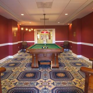 A well-decorated game room featuring a pool table, surrounded by red walls and patterned carpeting.