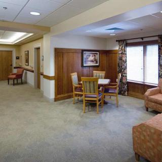 A comfortable lounge area with chairs and a table set on a carpeted floor, featuring large windows and decorative elements.