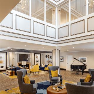 A modern lobby interior featuring a grand piano and comfortable seating under a bright atrium.