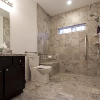 A modern and spacious bathroom with neutral-toned tiles, featuring a shower, toilet, and vanity unit.