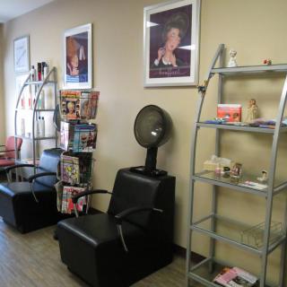 A cozy hair salon interior featuring a waiting area with chairs, magazines, and wall-mounted posters.