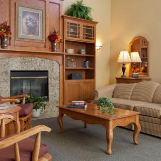 A cozy living room featuring comfortable seating, a central coffee table, and a warm fireplace surrounded by wooden furnishings.