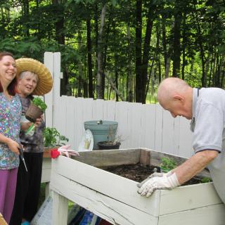 A group of people enjoying gardening together in a raised bed outdoors.