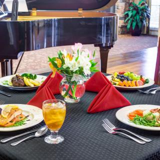 Elegant dining table setup with meals, red napkins, and a piano in the background.