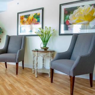 A cozy and stylish interior featuring two gray upholstered chairs, adorned with floral artwork and a small table with decorative plants.